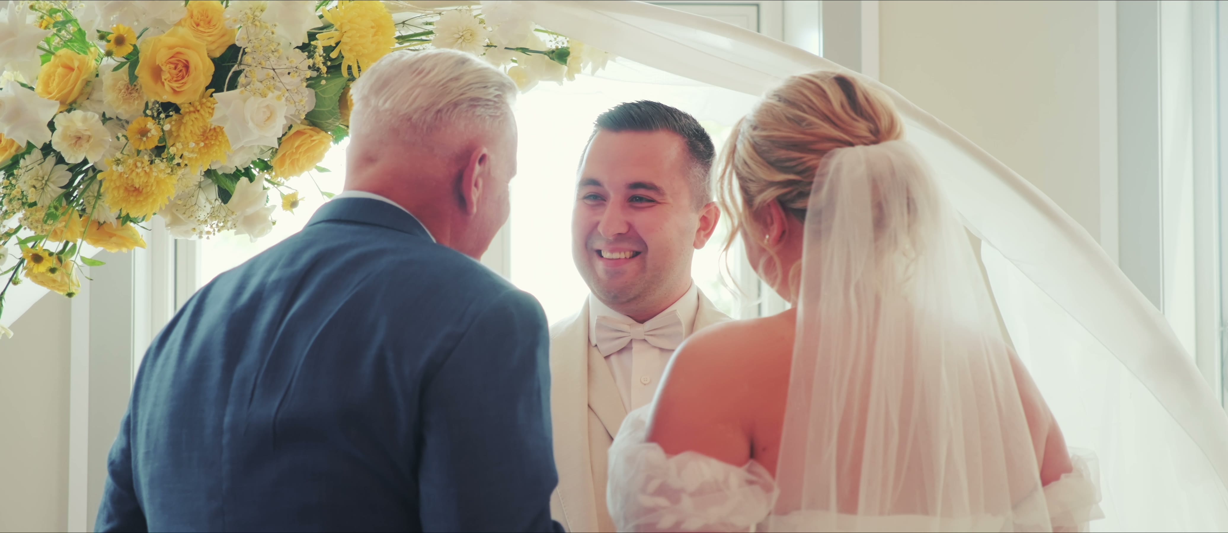 Hochzeits-Aftermovie – Referenz Standbild aus dem Hochzeits-Aftermovie: Brautpaar und Trauzeuge lachen während der freien Trauung